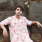 Man posing on rocks wearing a trendy oversized casual shirt in light colors with unique patterns