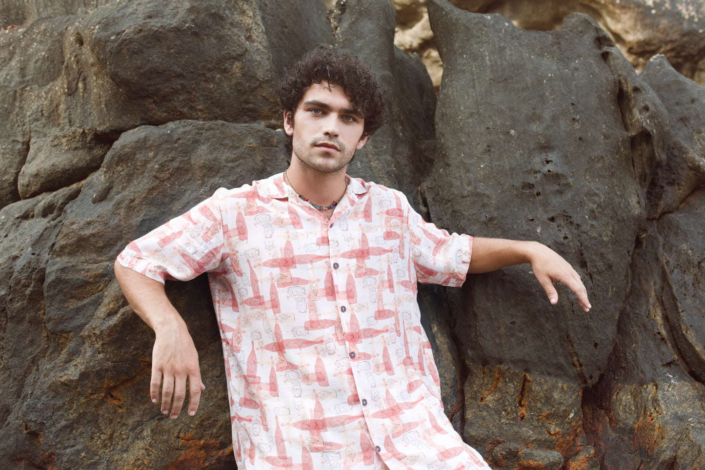 Man posing on rocks wearing a trendy oversized casual shirt in light colors with unique patterns