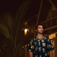 Man wearing a Stylera trendy oversized shirt for men with colorful print against a tropical backdrop