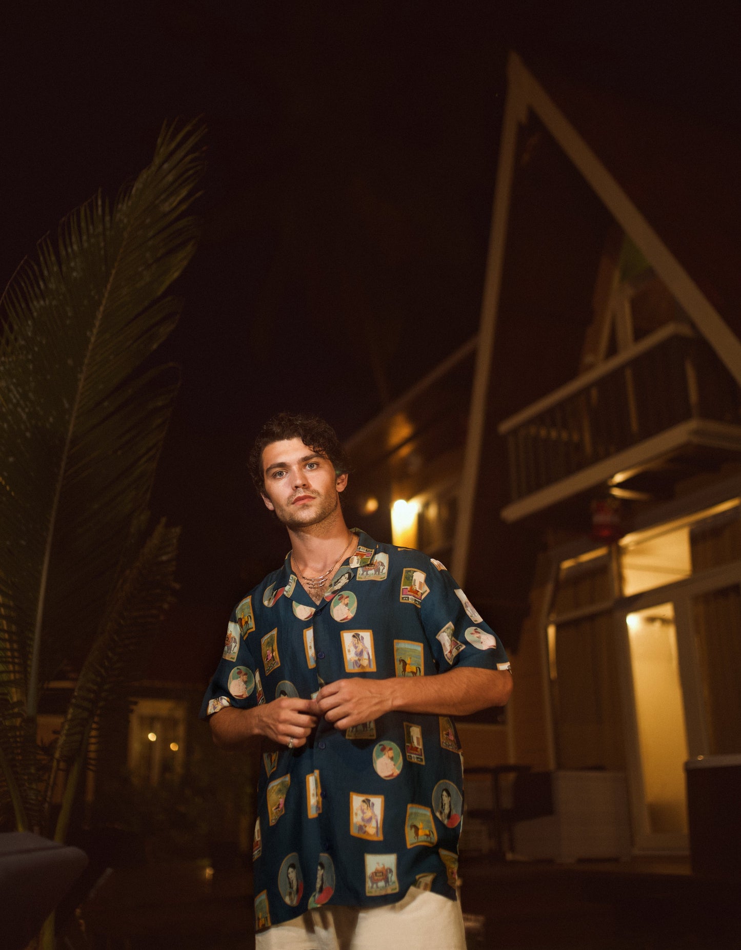 Man wearing a trendy oversized shirt for men with colorful prints, standing outdoors at night