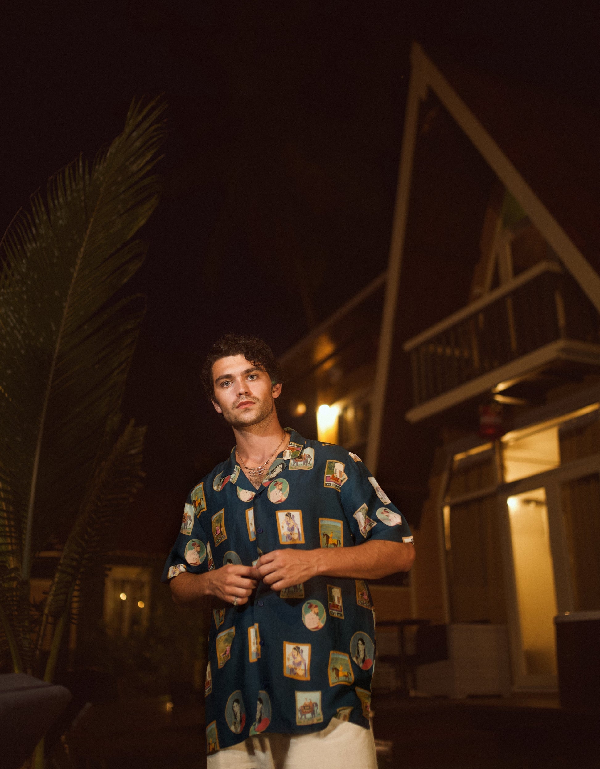Man wearing a trendy oversized shirt for men with colorful prints, standing outdoors at night