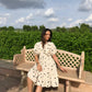 Chic model in a trendy polka dots midi dress sitting on a bench in a lush outdoor setting