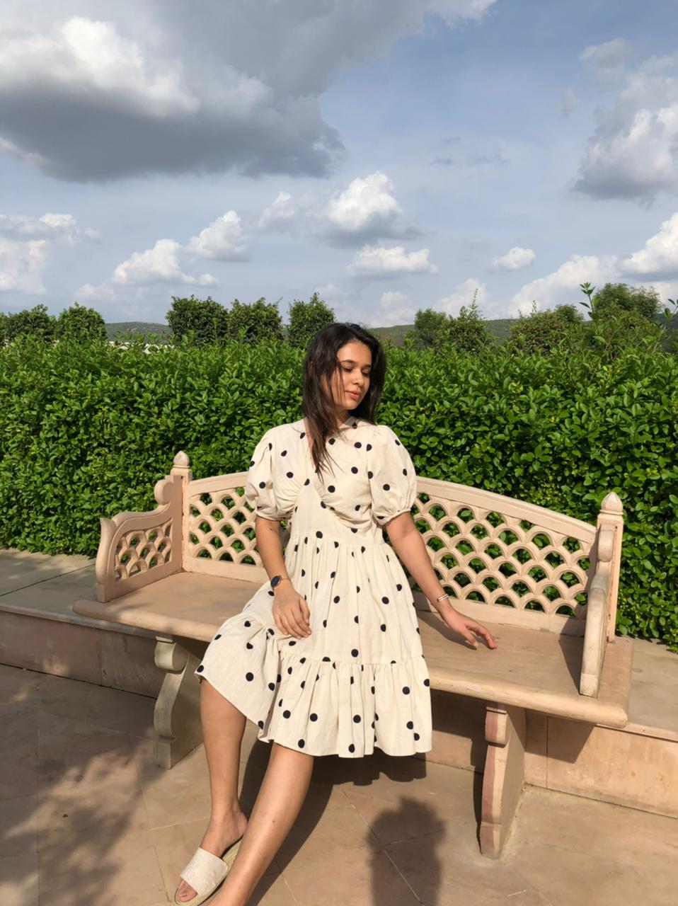Chic model in a trendy polka dots midi dress sitting on a bench in a lush outdoor setting