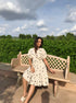 Chic model in a trendy polka dots midi dress sitting on a bench in a lush outdoor setting
