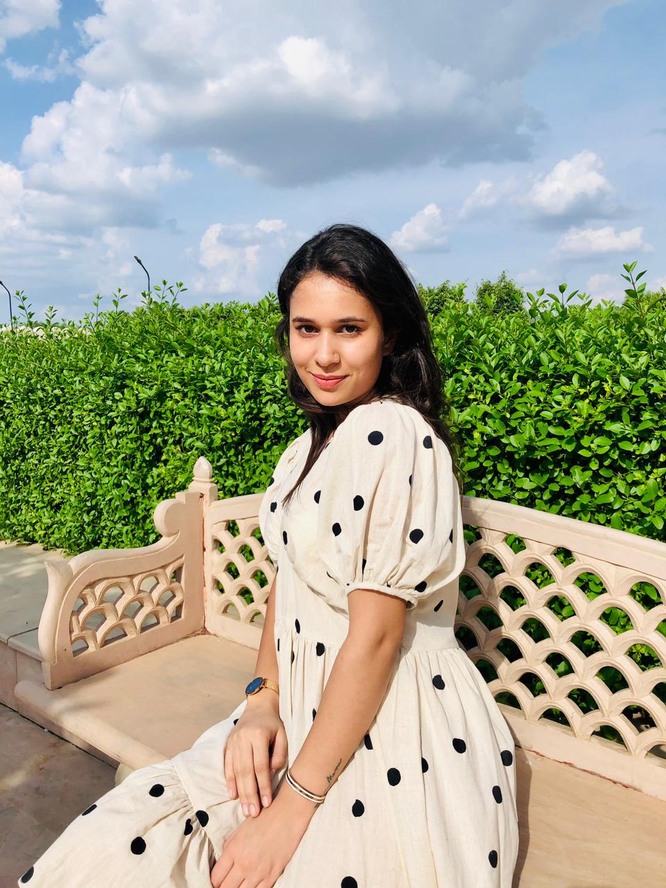 Model wearing a trendy polka dots midi dress sitting on a bench surrounded by greenery
