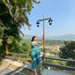 Model wearing a trendy printed two piece set, sitting on a railing with a scenic mountain view