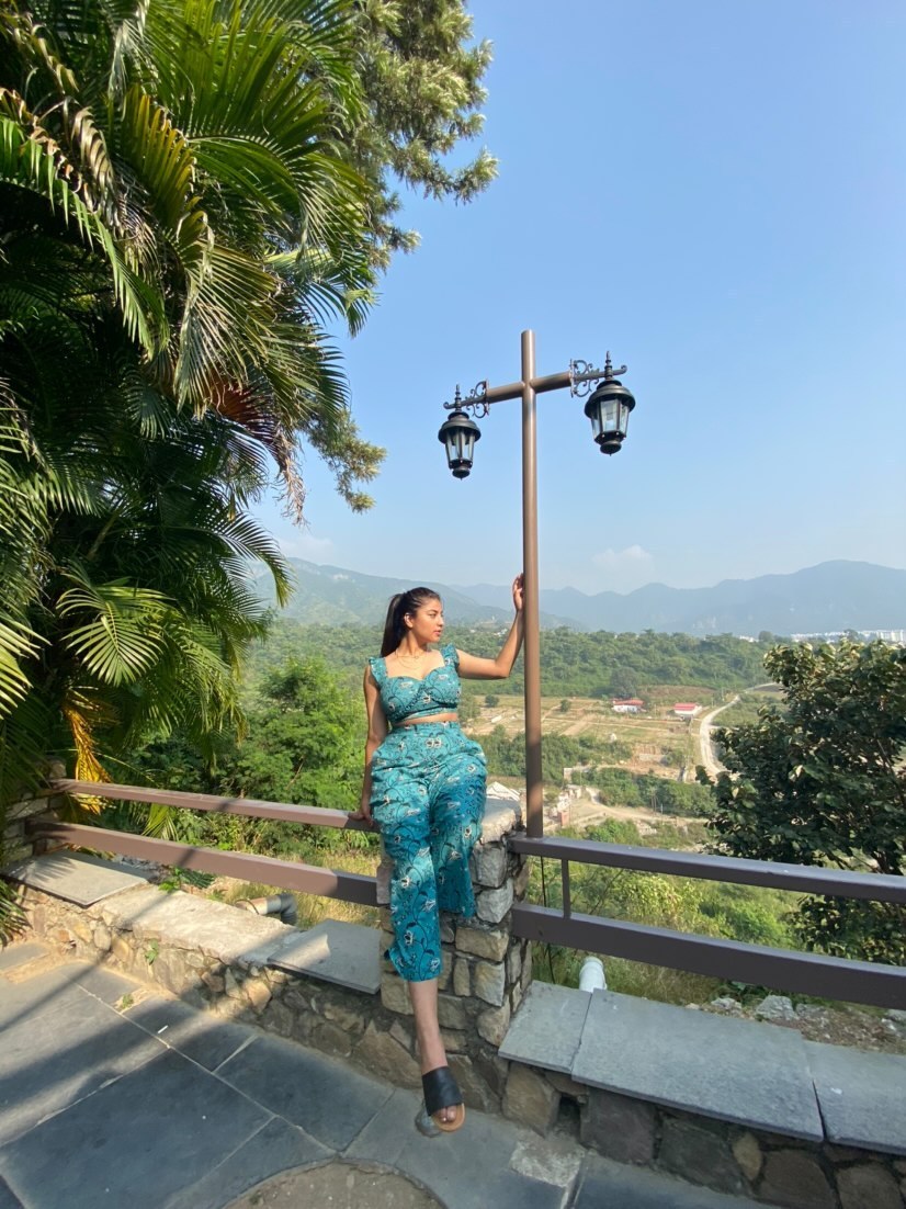 Model wearing a trendy printed two piece set, sitting on a railing with a scenic mountain view