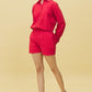 Model wearing trendy red matching shorts and shirt set with long sleeve button shirt and casual sneakers