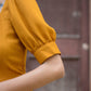 Detail of a trendy yellow slit midi dress featuring puff sleeves and a stylish neckline