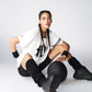 A woman in sportswear with braids sits on the floor wearing the Oversize Fly Tee, confidently holding a basketball and looking at the camera.