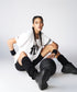 A woman in sportswear with braids sits on the floor wearing the Oversize Fly Tee, confidently holding a basketball and looking at the camera.
