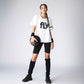 A young woman in a sporty outfit holds a basketball, wearing the Oversize Fly Tee with bold "FLY" print, black shorts, and long socks. The 100% cotton Oversize Fly Tee offers comfort both on and off the court.