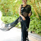 Elegant woman in a unique black saree for party wear, walking gracefully in a lush garden
