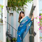 Elegant woman in a unique blue saree for special occasions, adorned with floral patterns, standing in a beautiful entryway