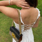 Back view of a woman wearing a unique casual dress with a lace-up design, paired with a stylish handbag
