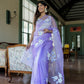 Elegant woman wearing a unique organza saree with artwork in soft lavender, styled for a chic indoor setting.