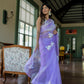 Elegant woman in a unique organza saree with artwork, standing indoors with floral designs