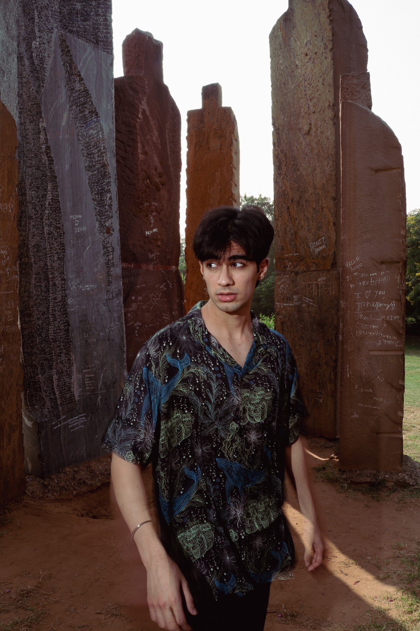 Young man wearing a unique print casual shirt surrounded by artistic stone pillars
