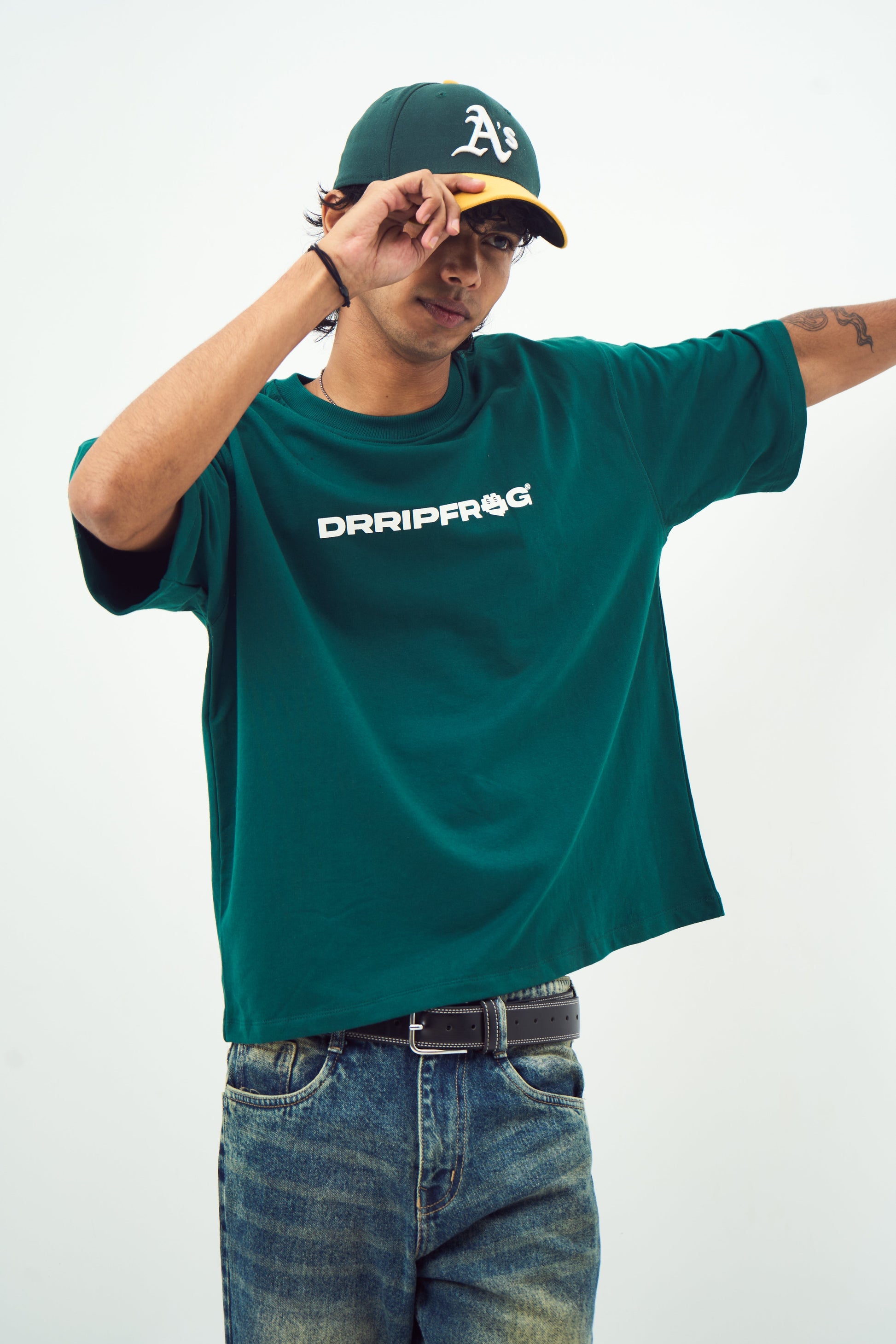 Young man wearing Stylera unisex oversized green t-shirt with white logo paired with baseball cap and jeans
