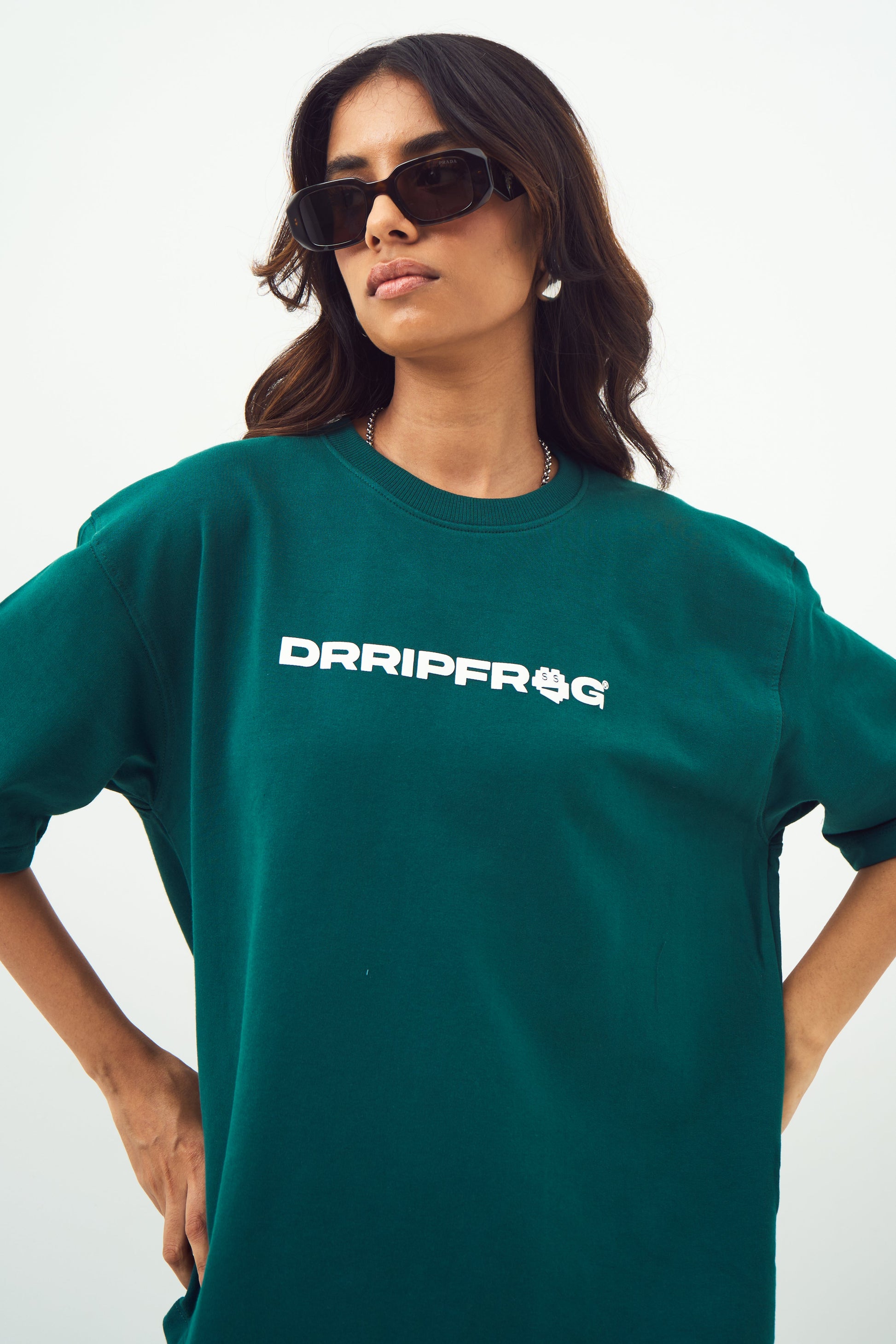 Model wearing Stylera unisex oversized green t-shirt with white logo sunglasses hands on hips casual look