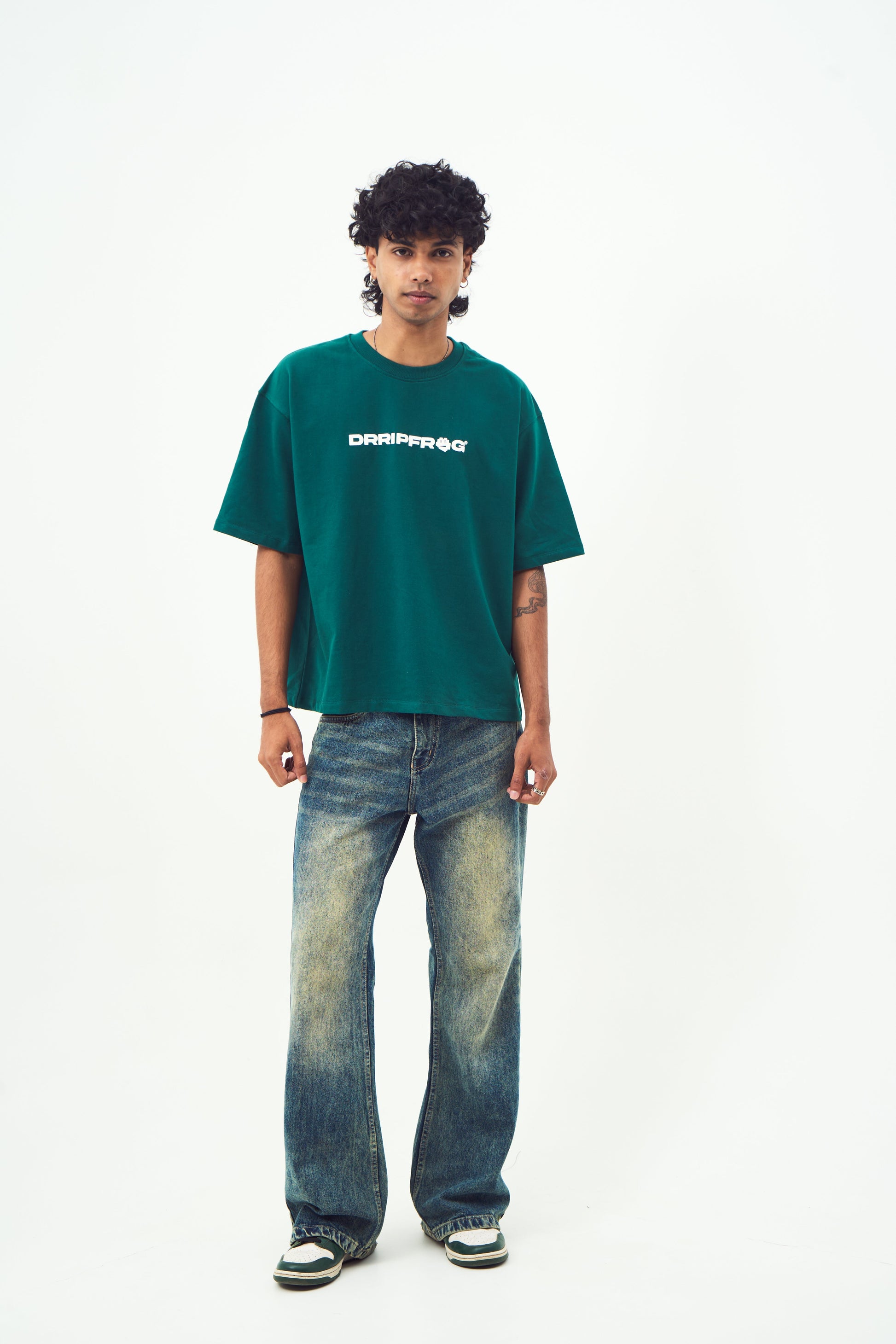 Male model wearing Stylera unisex oversized green t-shirt paired with faded jeans and sneakers standing