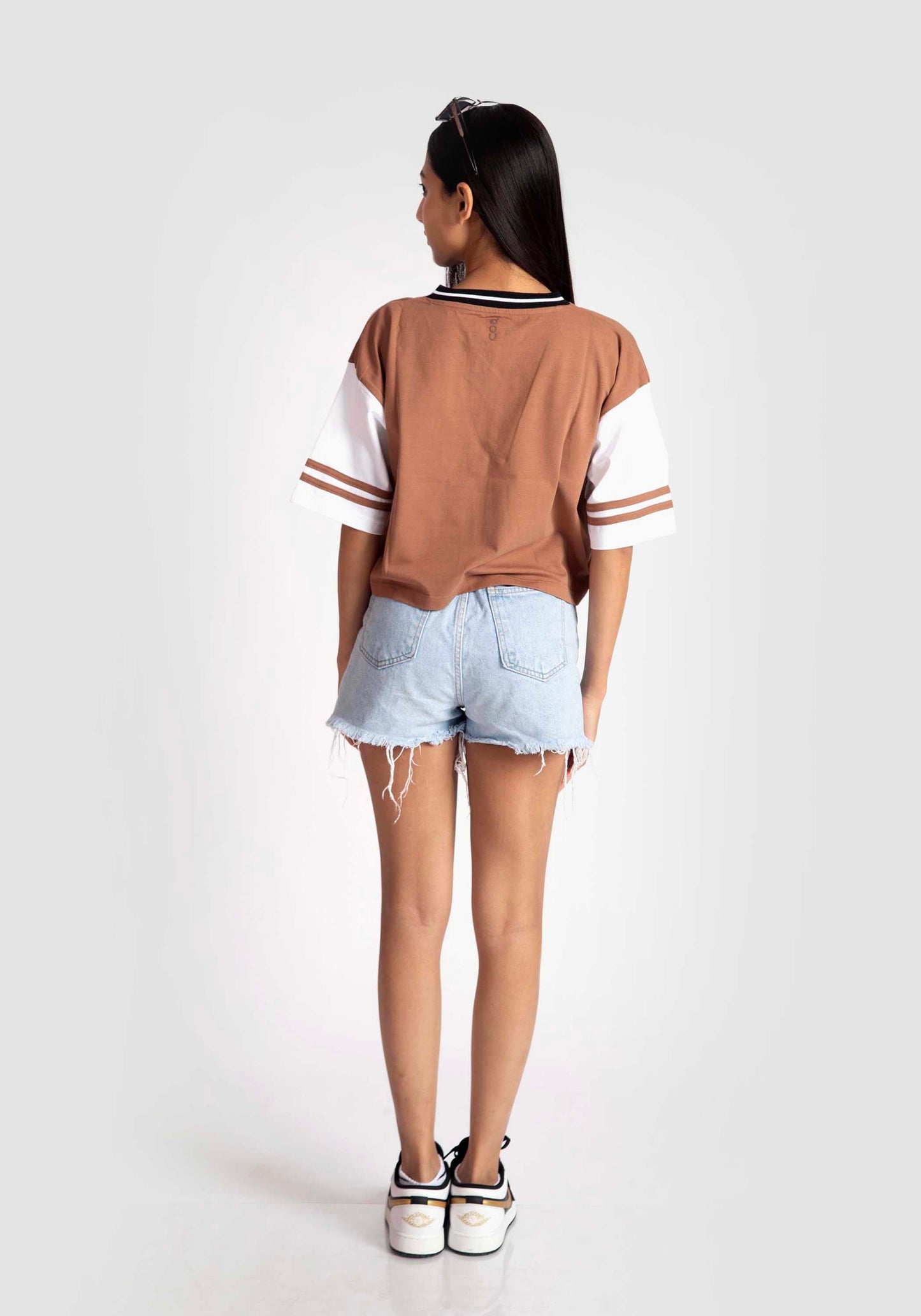 Back view of woman wearing brown and white graphic tee for women with striped sleeve details and denim shorts