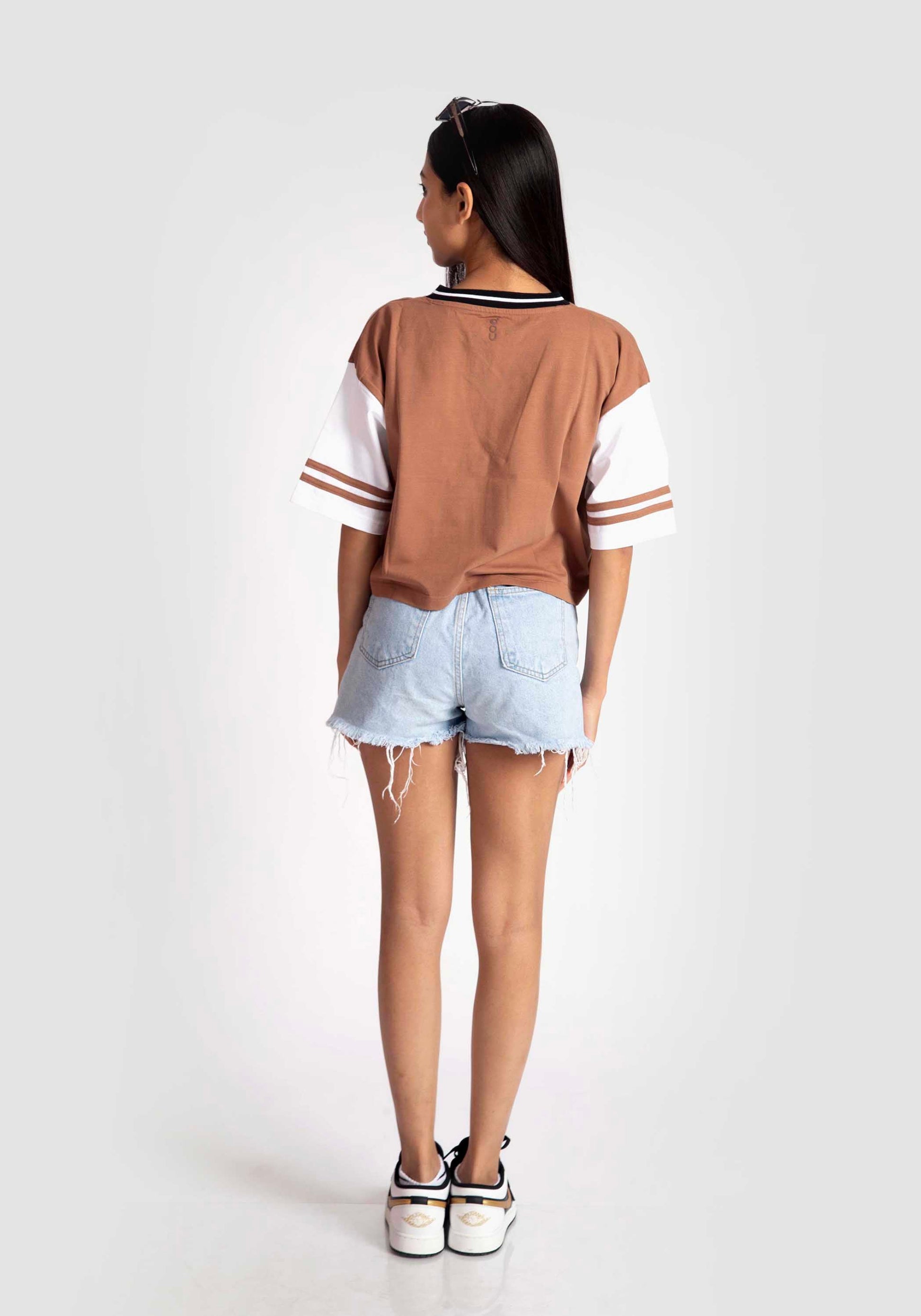 Back view of woman wearing brown and white graphic tee for women with striped sleeve details and denim shorts