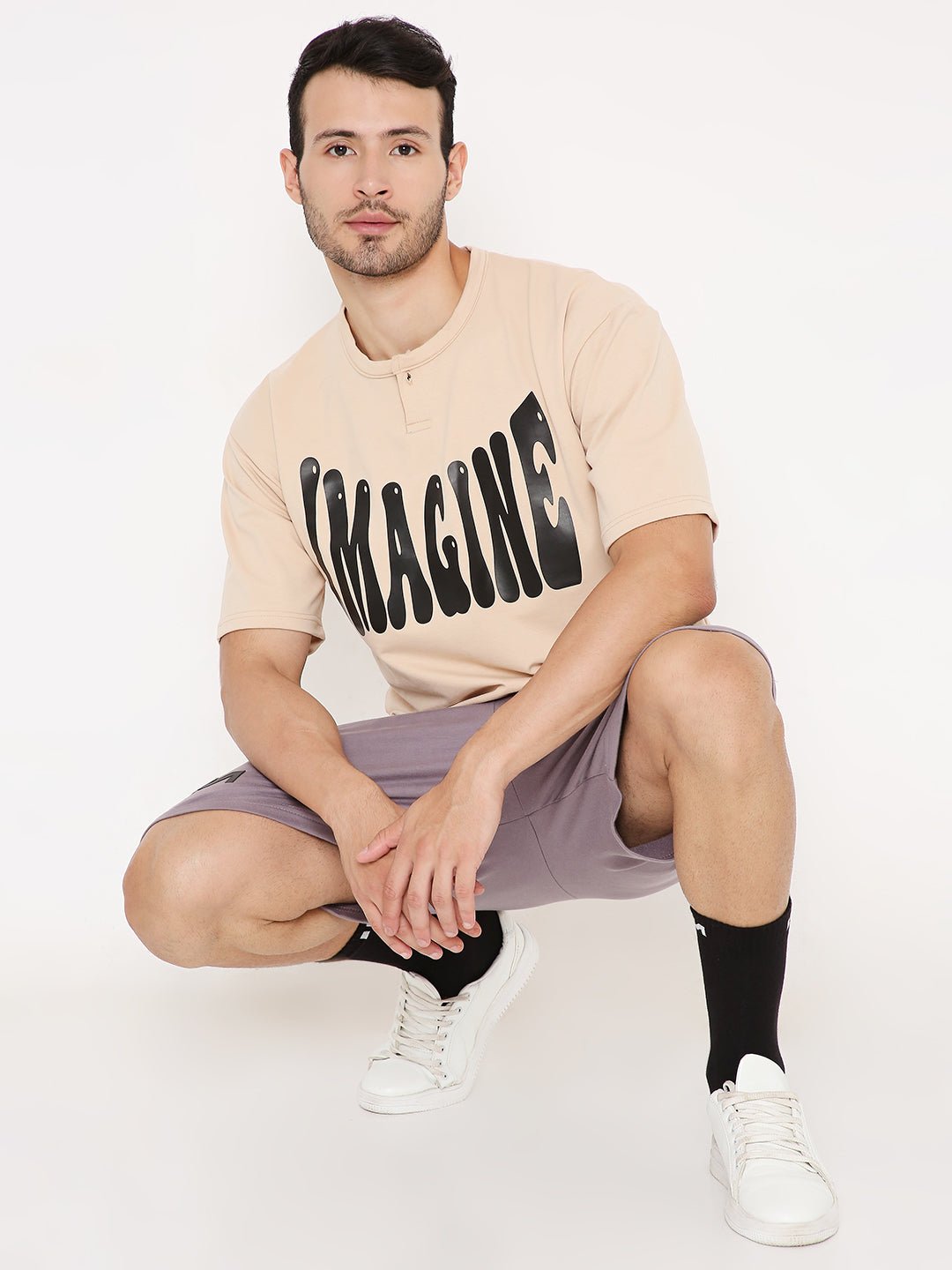 Stylera model wearing beige casual oversized t-shirt with print IMAGINE paired with shorts and white sneakers