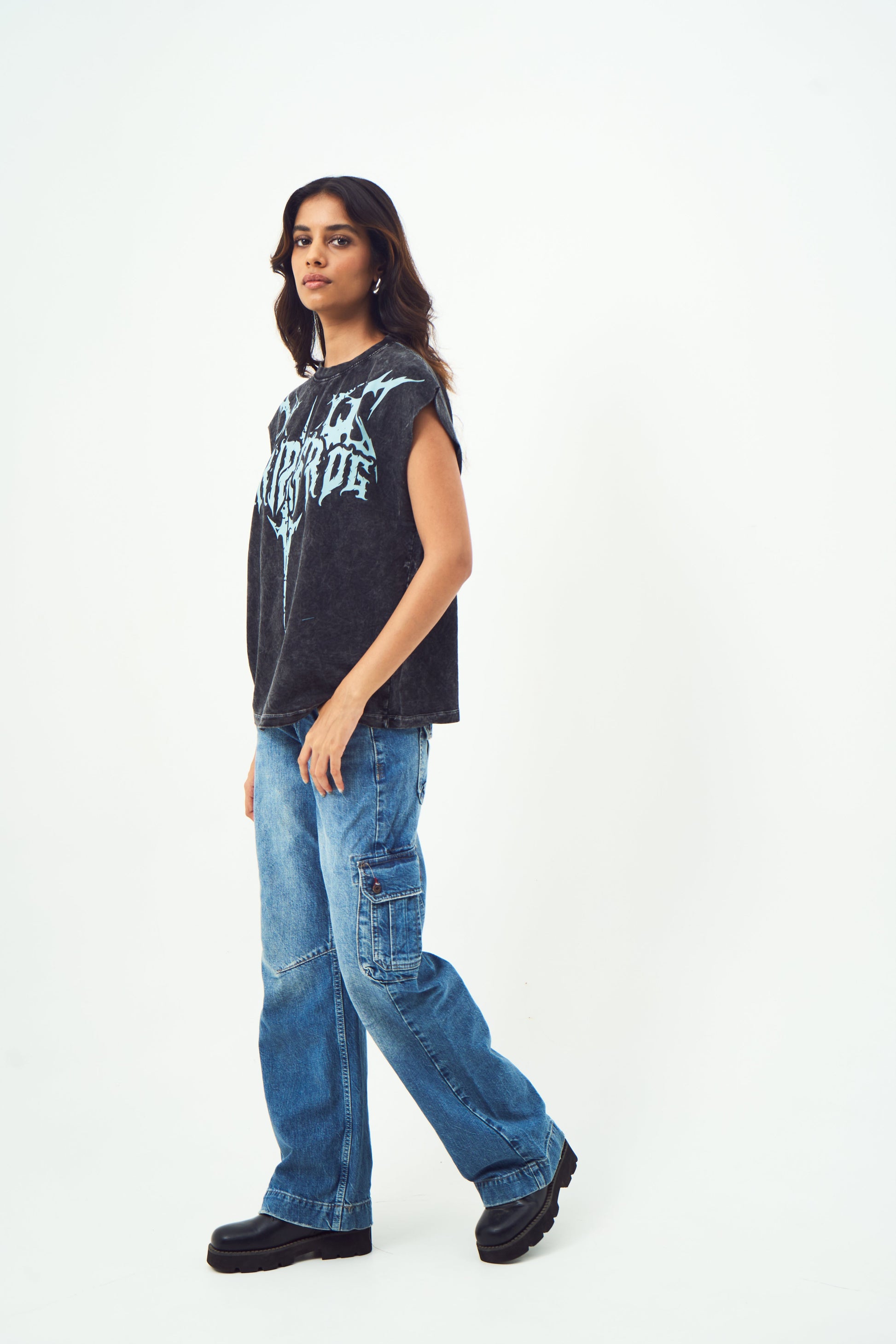 Model wearing Stylera unisex gothic print sleeveless top in faded black paired with baggy cargo jeans