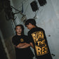 Stylera black graphic t-shirt trendy with bold yellow back print worn by two models in grunge setting