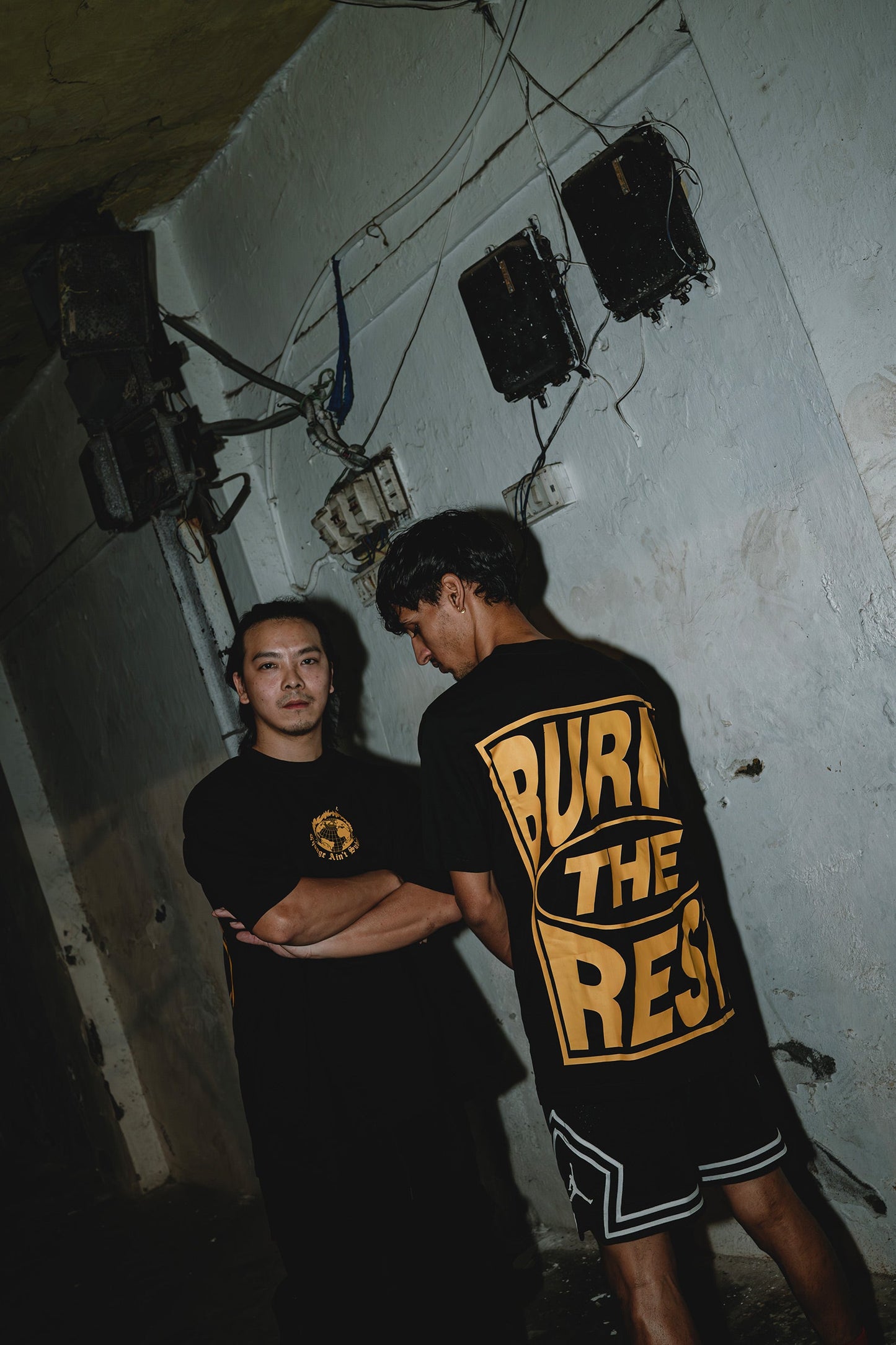Stylera black graphic t-shirt trendy with bold yellow back print worn by two models in grunge setting