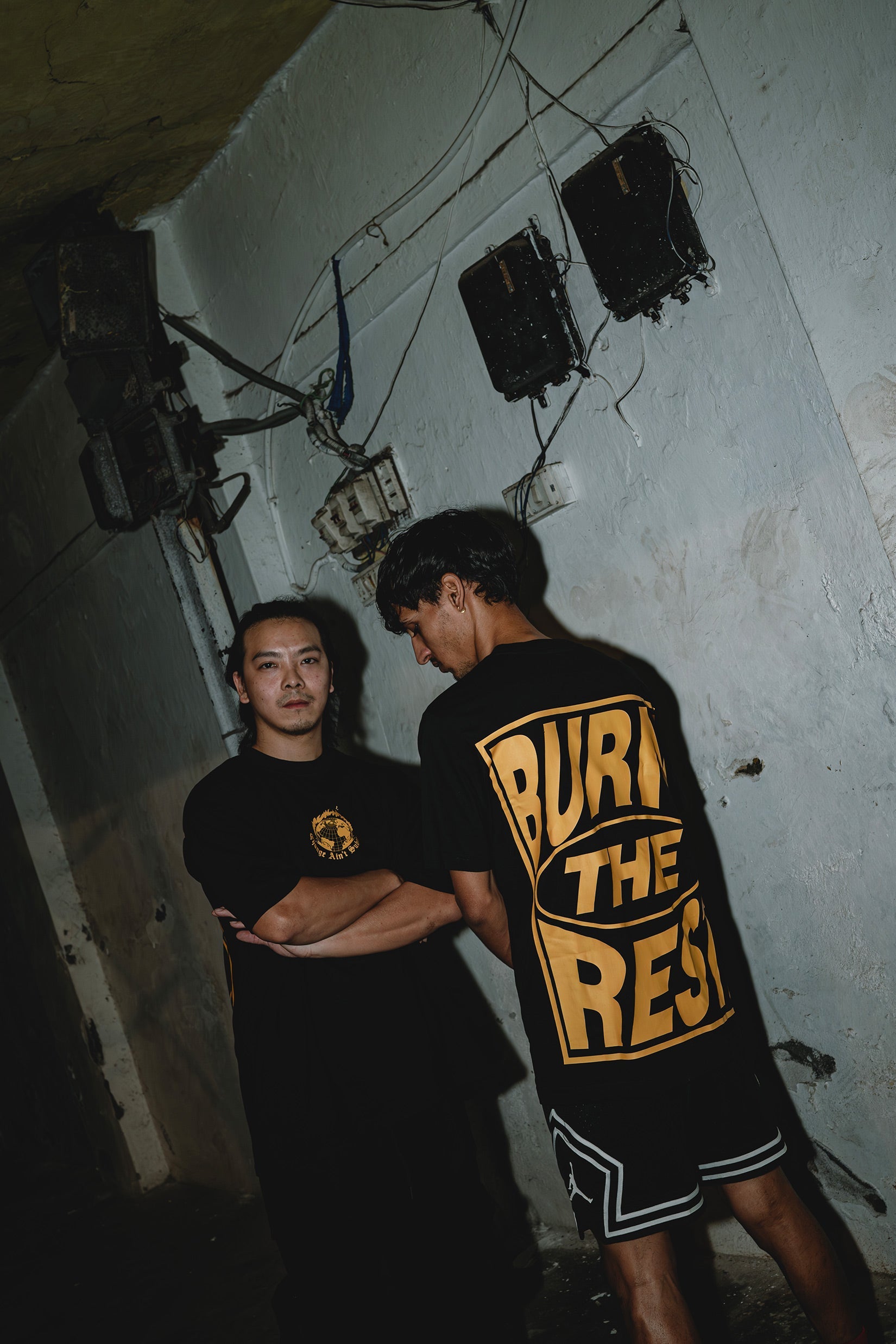Stylera black graphic t-shirt trendy with bold yellow back print worn by two models in grunge setting