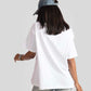 Back view of woman wearing a white good vibes only graphic tee for women with denim cap and light jeans