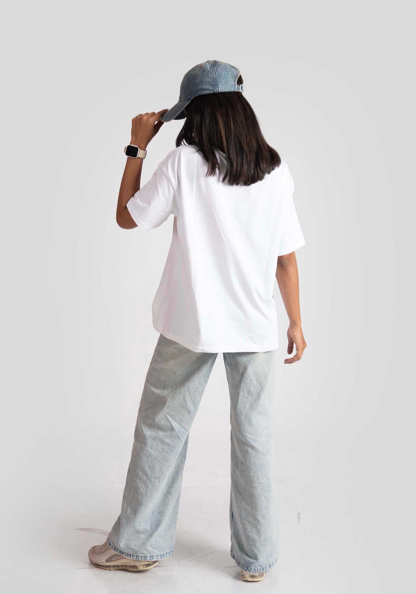 Woman wearing a white good vibes only graphic tee for women with light wash jeans and a blue cap