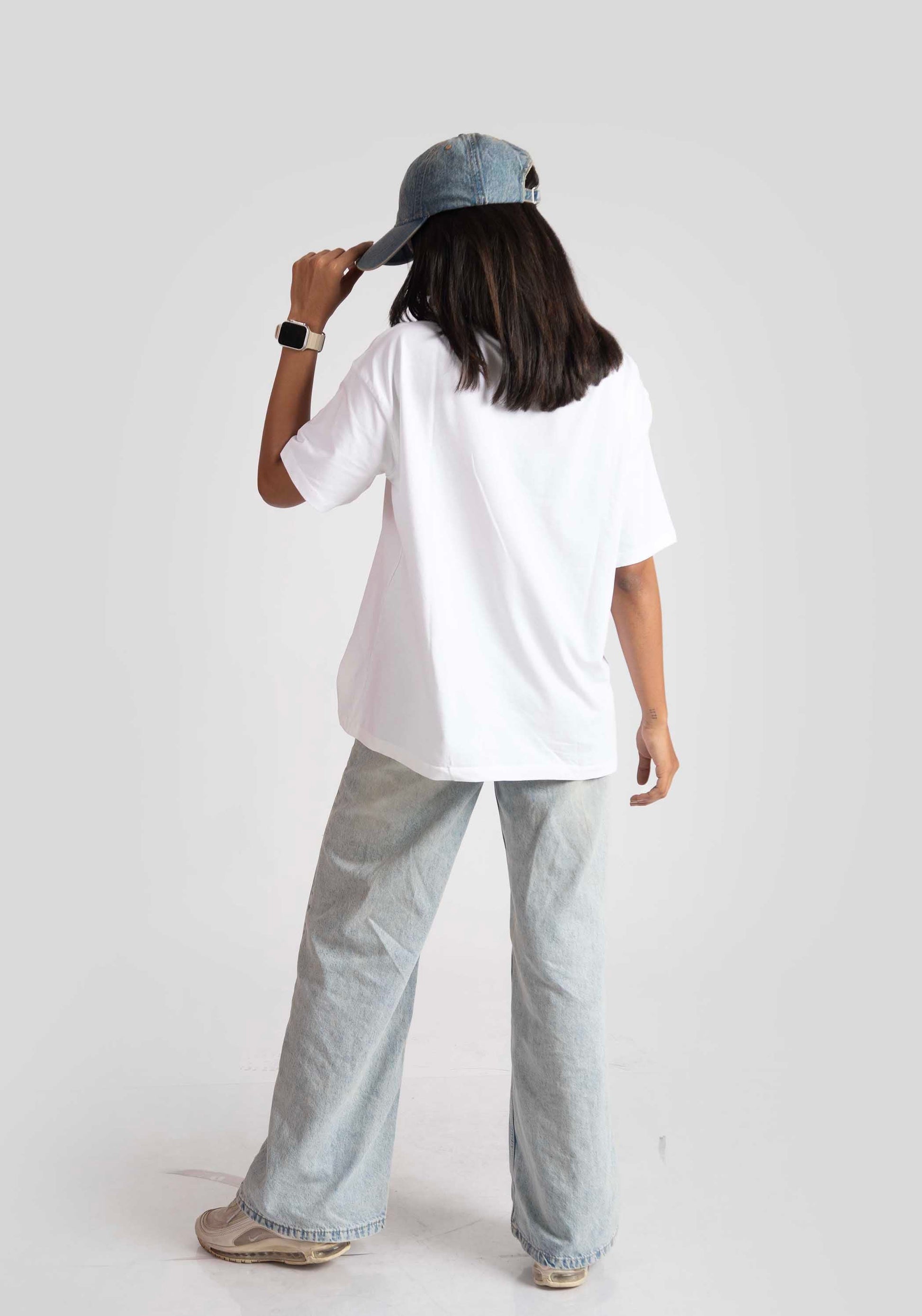 Woman wearing a white good vibes only graphic tee for women with light wash jeans and a blue cap