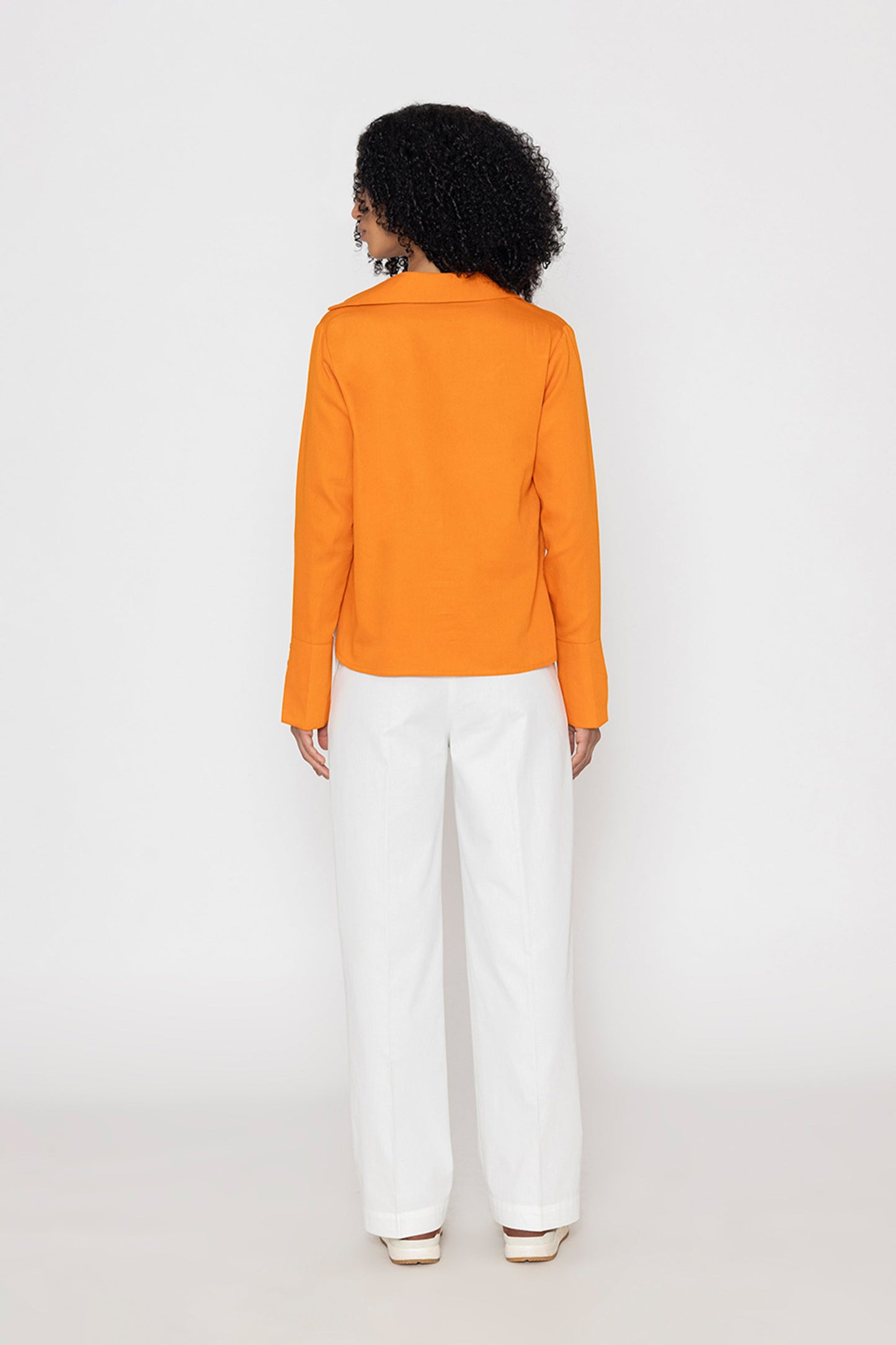 Back view of orange v-neck blouse for women paired with white wide-leg pants by Stylera