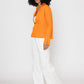 Stylera orange v-neck blouse for women styled with white wide-leg pants and sneakers