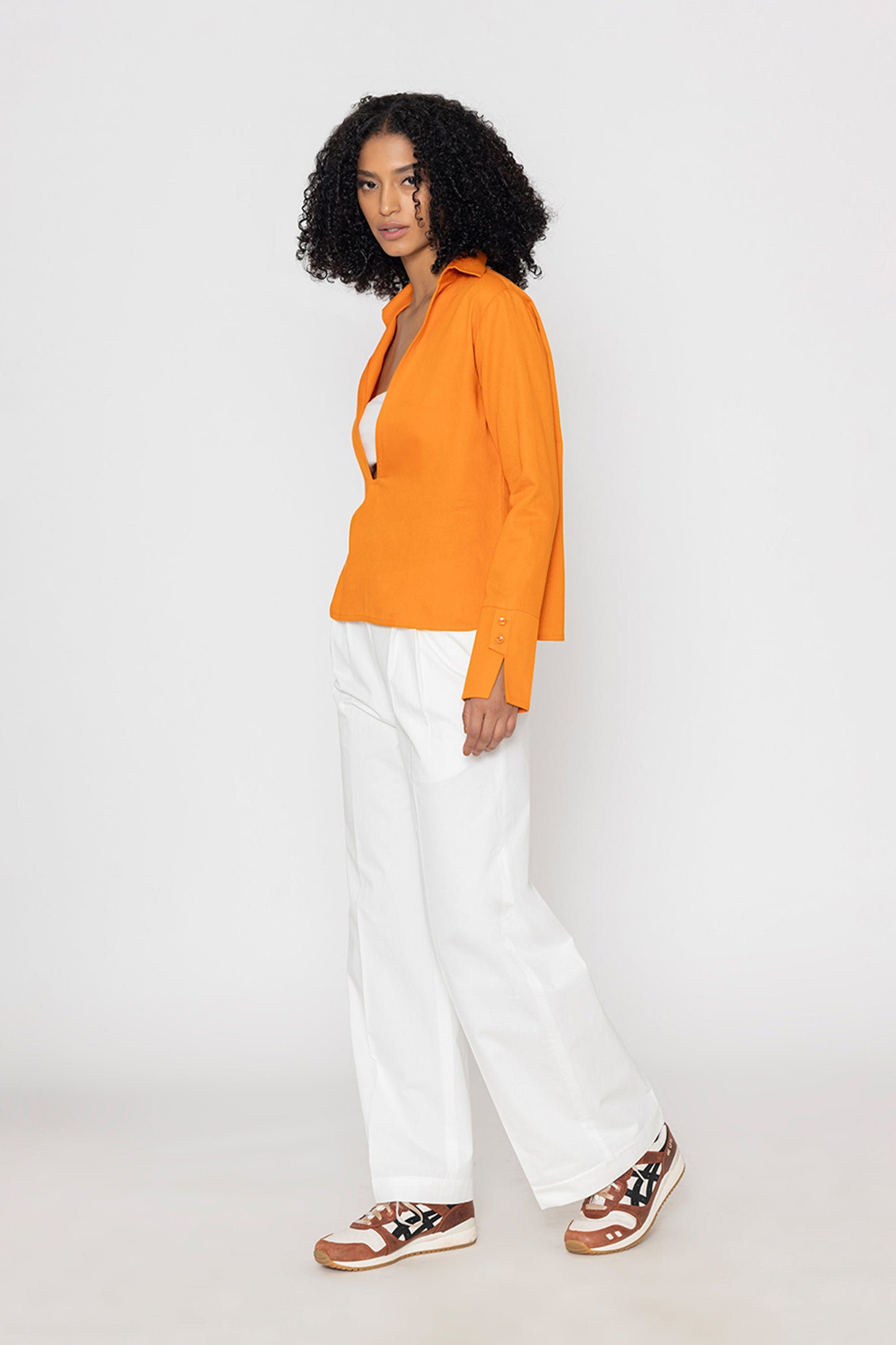 Stylera orange v-neck blouse for women styled with white wide-leg pants and sneakers