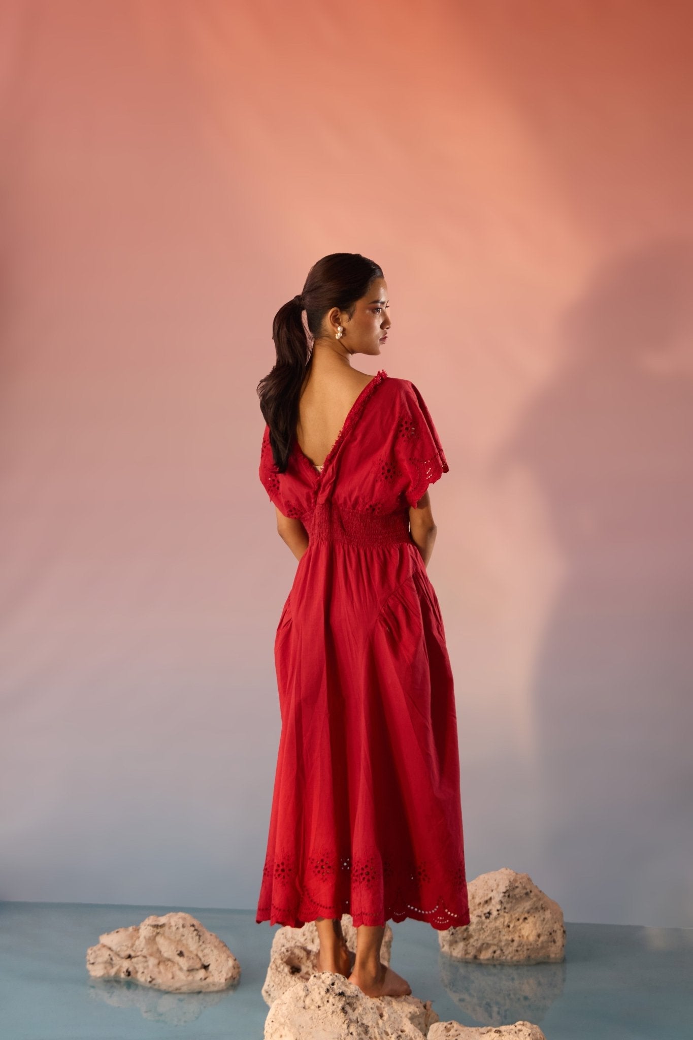 Stylera red Schiffli maxi dress with short sleeves and V-back on model standing on rocks