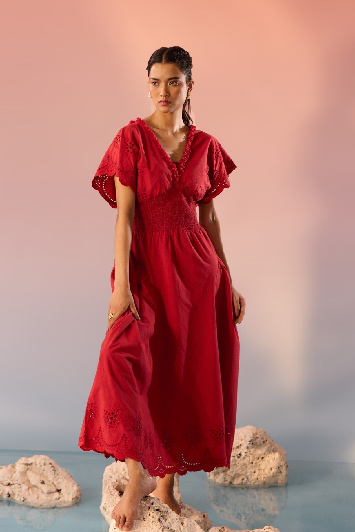 Stylera red Schiffli maxi dress with short sleeves and scalloped hem worn by model on rocks