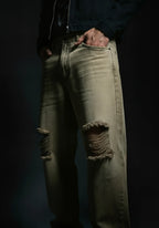 Person wearing distressed beige jeans against a dark background