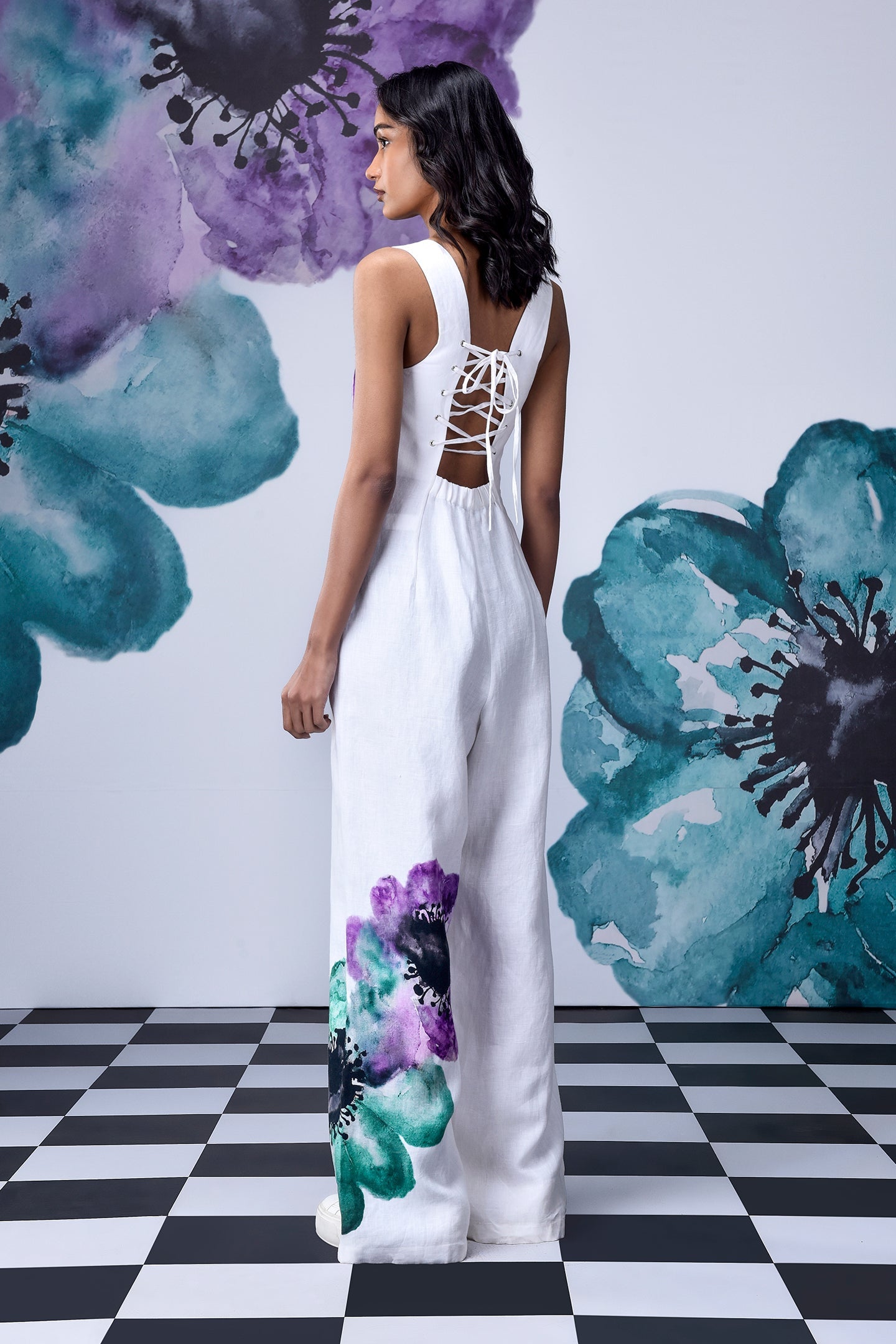 Model wearing white coral floral jumpsuit by Stylera with lace up back and watercolor floral print on leg