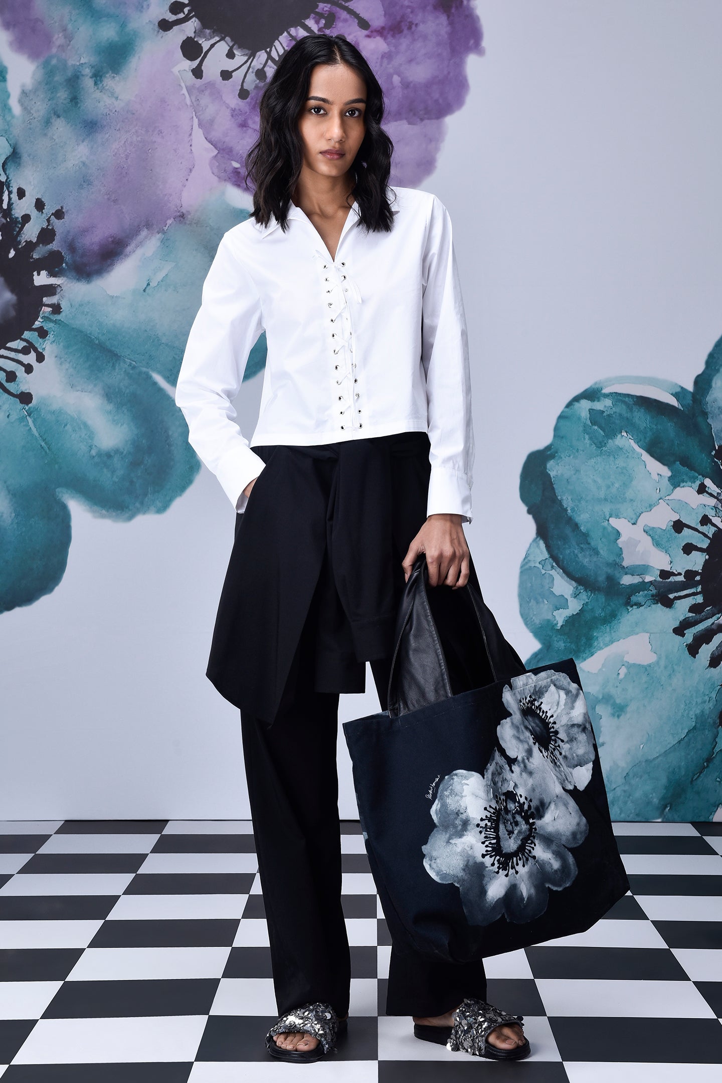 Model wearing Stylera white cotton lace up shirt paired with black wide pants and floral tote