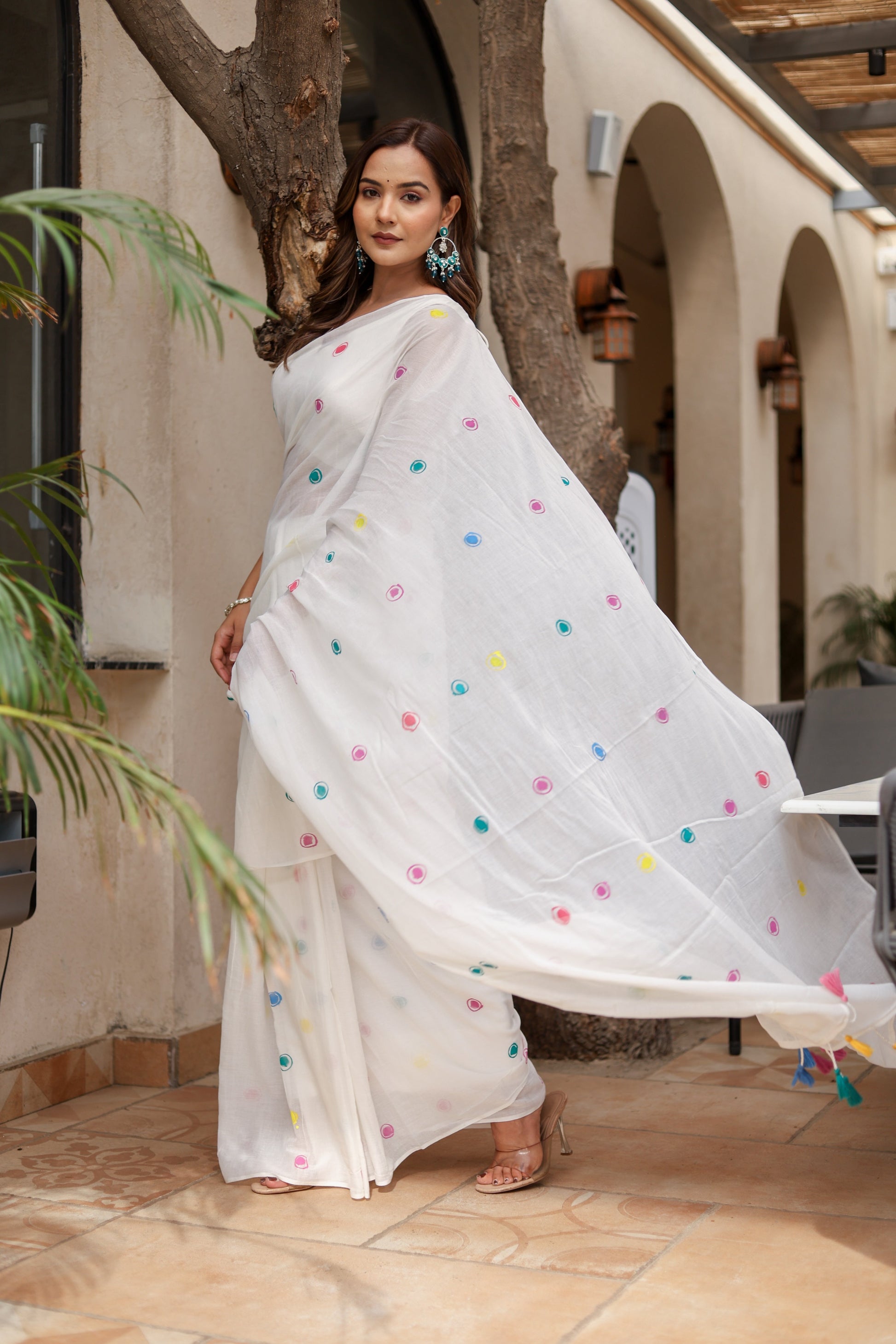 Elegant white cotton saree with tassels, featuring colorful floral motifs, perfect for festive occasions