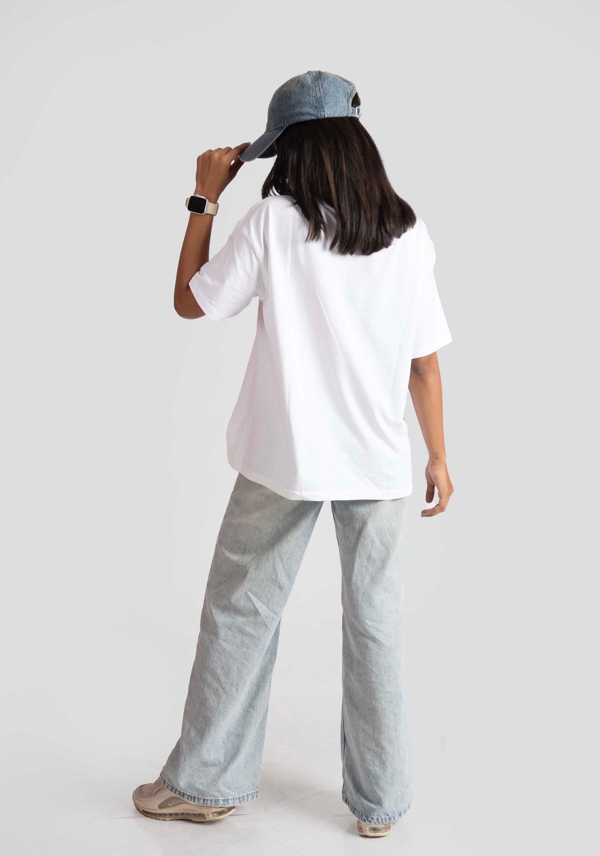 Back view of woman wearing white oversized anime t-shirt for women styled with wide-leg jeans and denim cap