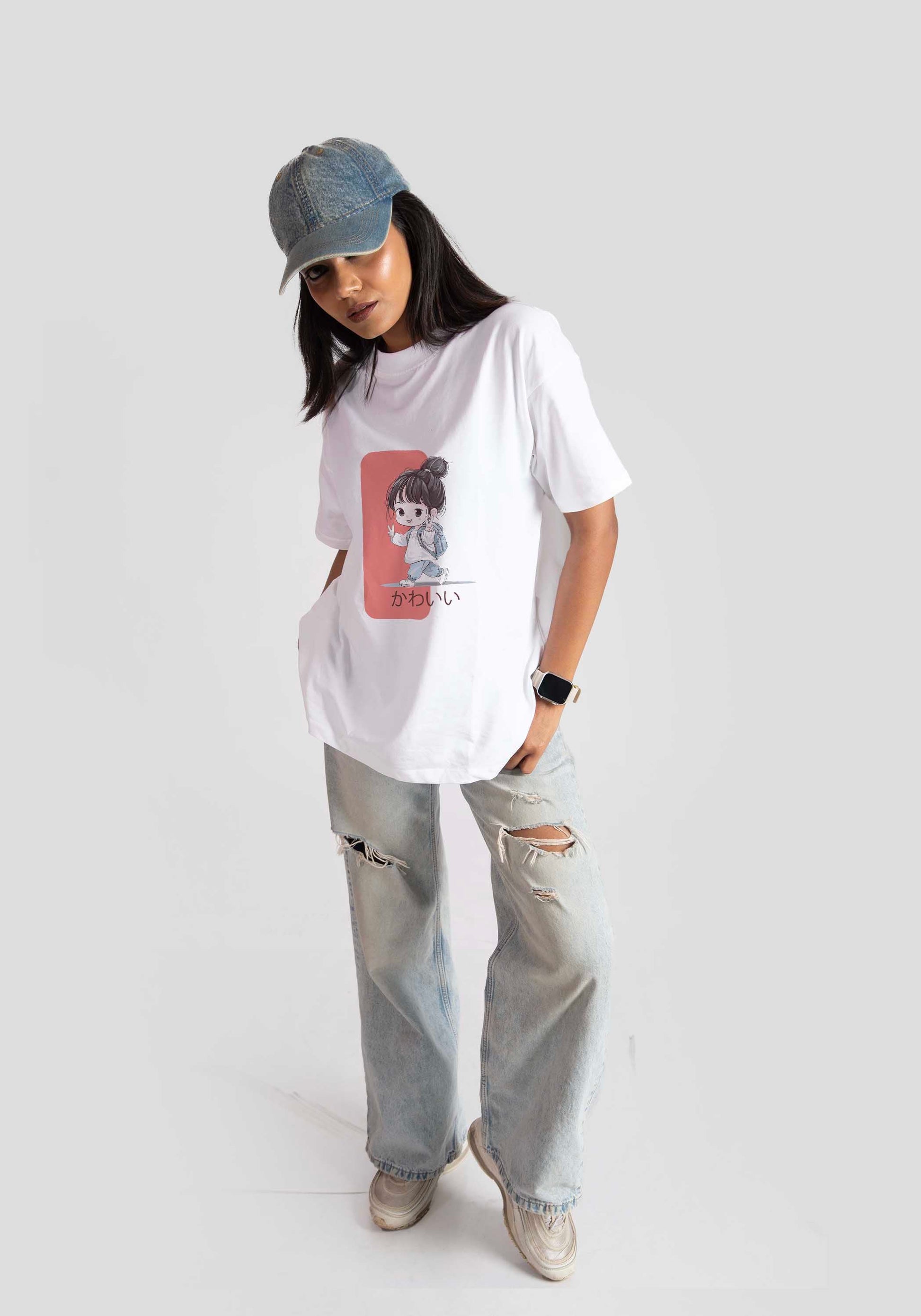 Woman wearing white oversized anime t-shirt for women with cartoon graphic, paired with ripped jeans and a denim cap