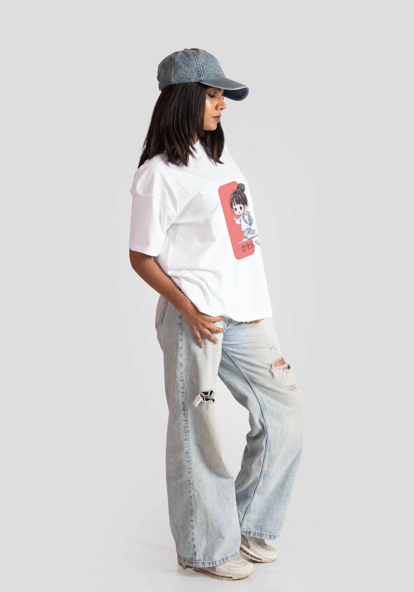 White oversized anime t-shirt for women styled with light washed ripped jeans and blue denim cap