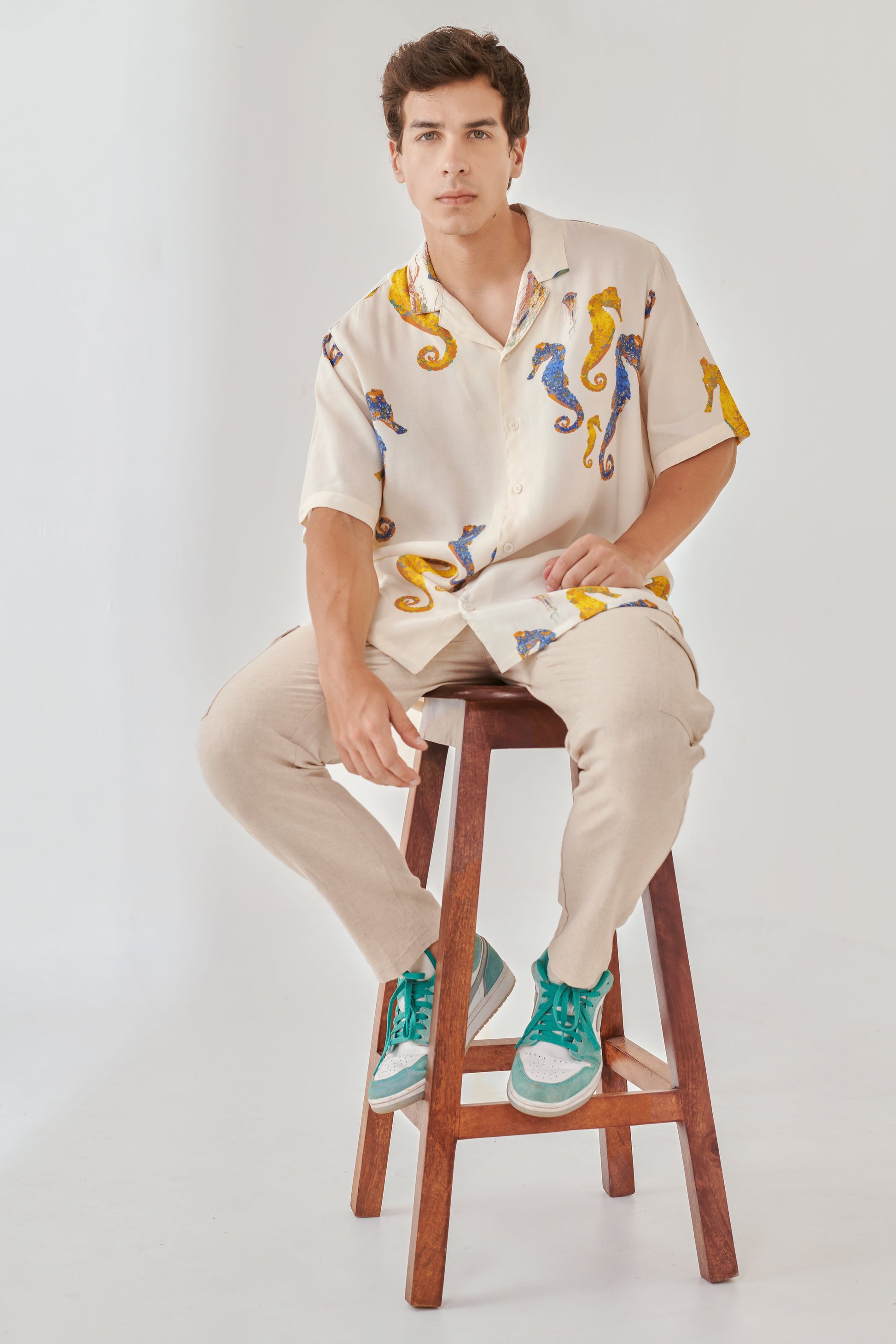 Casual model wearing a white oversized beach shirt men with colorful seahorse prints, paired with beige pants