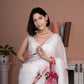 Elegant model wearing a white saree with pink floral print, styled with jewelry and a handbag