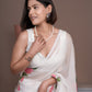 Elegant woman in a white saree with pink floral print, styled with pearls and earrings
